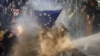GEORGIA -- Protesters brandishing a European Union flag are sprayed by a water cannon during clashes with riot police near the Georgian parliament in Tbilisi on March 7, 2023.