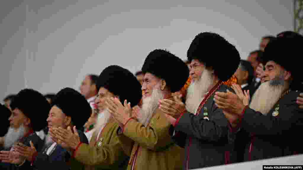 Аксакалы &mdash; мужчины-старейшины &mdash; аплодируют, наблюдая за празднеством с трибуны. И Бердымухамедов-старший, и его предшественник Сапармурат Ниязов построили культы личности, которые включают тщательно продуманные подношения и памятники
