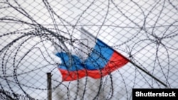 A Russian flag flies behind a fence and barbed wire. (Illustrative photo)
